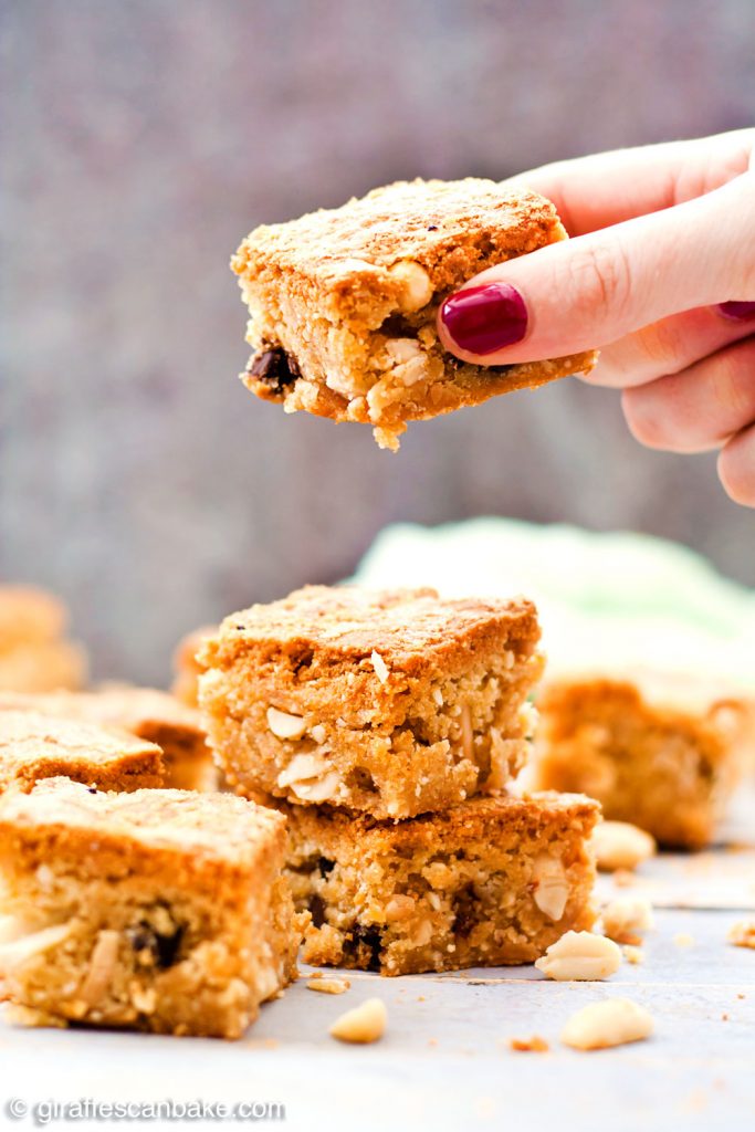 Gluten Free Triple Peanut Blondies - Chewy, moist and packed full of delicious peanut goodness. A peanut butter lover's dream come true! - Taking a blondie from the pile