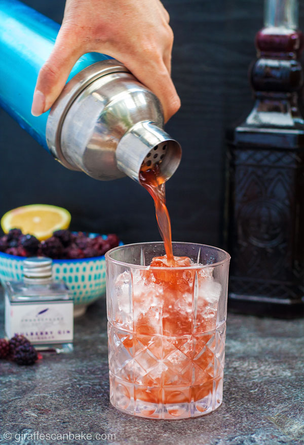 The Mulberry Bramble Cocktail being poured from a shaker into a glass filled with ice