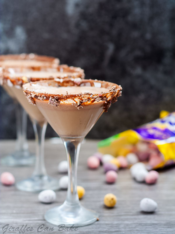 Mini Egg Chocolate Martini - three martini glasses in diagonal row filled with chocolate coloured liquid with bag of mini eggs spilling in background