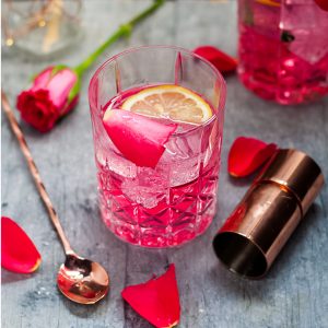 Rose Vodka Tonic Mixed Drink Cocktail - above view of cocktail in rocks glass with rose, jigger and stirrer surrounding, square cropped